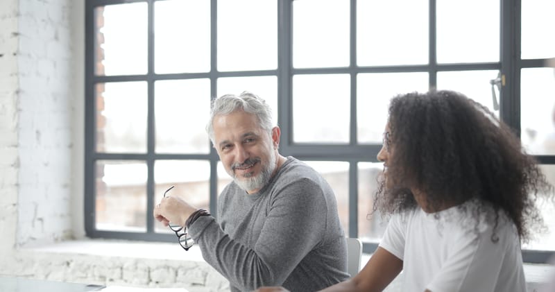 Cheerful senior gray haired mentor supporting young black colleague in office